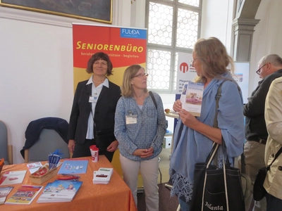 Drei Personen im Gespräch an einem Stand